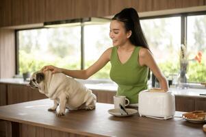 asiatique femme en train de préparer café et pain grillé pain pour petit déjeuner prendre plaisir avec chien à le cuisine table dans le Matin photo