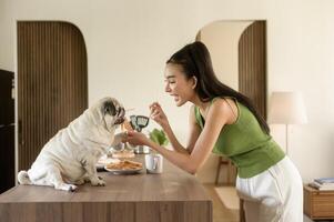 asiatique femme en train de préparer café et pain grillé pain pour petit déjeuner prendre plaisir avec chien à le cuisine table dans le Matin photo