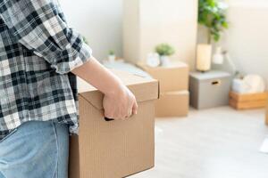 en mouvement loger, déménagement. femme tenir carton boîte contenir équipement pour Nouveau condominium, à l'intérieur le pièce a été une papier carton boîte contenant personnel affaires et meubles. bouge toi dans le appartement photo