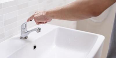 enregistrer l'eau. homme garde tournant de le fonctionnement l'eau dans le salle de bains à protéger environnement. écologisation planète, réduire global échauffement, enregistrer monde, vie, avenir, risque énergie, crise , l'eau journée. photo