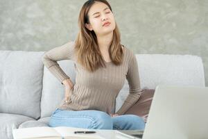 Asie magnifique femme en portant sa inférieur retour tandis que et souffrir de insupportable douleur santé et problèmes, chronique retour douleur, mal au dos dans Bureau syndrome, scoliose, hernie disque, muscle inflammation photo