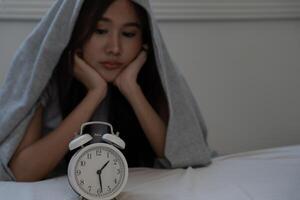 asiatique femme dans lit en retard en essayant à sommeil Souffrance insomnie, sans sommeil ou effrayé dans une cauchemar, à la recherche triste inquiet et stressé. fatigué et mal de crâne ou migraine veille en haut dans le milieu de le nuit. photo