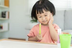 peu asiatique fille presses main à joue, souffre de douleur dans dent. les dents carie, dentaire problèmes, enfant émotions et faciale expression, oral santé se soucier, réduire bonbons, fluor enrobage photo