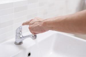 enregistrer l'eau. homme garde tournant de le fonctionnement l'eau dans le salle de bains à protéger environnement. écologisation planète, réduire global échauffement, enregistrer monde, vie, avenir, risque énergie, crise , l'eau journée. photo