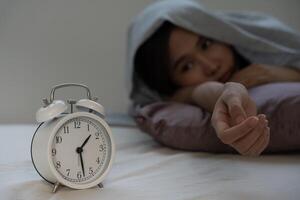 asiatique femme dans lit en retard en essayant à sommeil Souffrance insomnie, sans sommeil ou effrayé dans une cauchemar, à la recherche triste inquiet et stressé. fatigué et mal de crâne ou migraine veille en haut dans le milieu de le nuit. photo