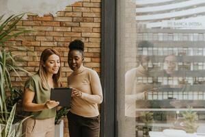 deux Jeune affaires femmes avec numérique tablette permanent par le brique mur dans le industriel style Bureau photo