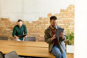 engagé collègues dans une moderne espace de travail, réflexion avec tablette et portable photo