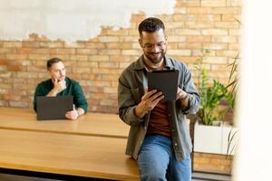 engagé collègues dans une moderne espace de travail, réflexion avec tablette et portable photo