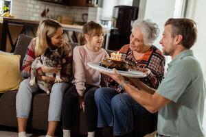 joyeux famille célébrer grands-mères anniversaire avec gâteau dans une confortable vivant pièce photo