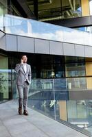 sur de soi homme d'affaire souriant dans tranchant costume contre moderne verre Bureau façade photo