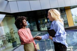 deux professionnel femmes partage une joyeux conversation à une moderne Bureau bâtiment photo