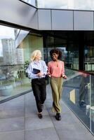 deux professionnel femmes partage une joyeux conversation à une moderne Bureau bâtiment photo