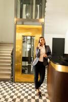 femme d'affaires sortir ascenseur dans moderne Bureau hall pendant une téléphone conversation. génératif ai photo