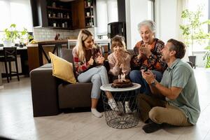 joyeux famille célébrer grands-mères anniversaire avec gâteau dans une confortable vivant pièce photo