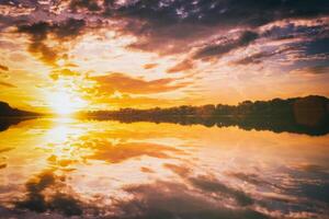 lever du soleil ou le coucher du soleil sur une Lac ou rivière avec nuageux ciel réflexion dans le l'eau dans heure d'été. esthétique de ancien film. photo