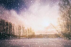 le coucher du soleil ou lever du soleil sur une congelé étang avec bouleau des arbres le long de le banques et chute neige. chute de neige. ancien caméra film esthétique. photo