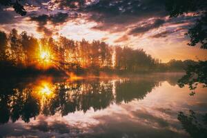 Aube sur une Lac ou rivière avec une ciel réfléchi dans le eau, bouleau des arbres sur le rive et le rayons de soleil rupture par leur et brouillard dans l'automne. esthétique de ancien film. photo