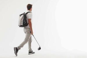 le golf joueur dans une blanc chemise en marchant avec une sac de le golf clubs sur le sien retour sur une blanc Contexte. photo