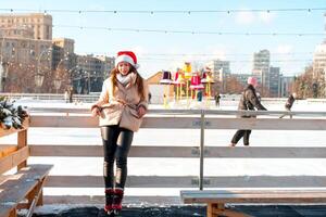 magnifique charmant Jeune adulte femme brunet cheveux chaud hiver vestes des stands près la glace patin patinoire Contexte ville carré. Noël ambiance mode de vie photo