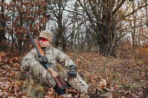 une Masculin chasseur avec une pistolet tandis que séance prend objectif à une forêt. le concept de une réussi chasse, un expérimenté chasseur. chasse le l'automne saison. le chasseur a une fusil et une chasse uniforme photo