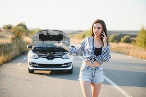 le Jeune fille cassé le voiture et elle ouvert le capuche et a essayé à réparation le voiture sur le route. une femme appels sur une téléphone intelligent avec une voiture évacuation un service photo