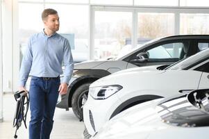 Jeune homme, vente électrique voitures dans le salle d'exposition. concept de achat respectueux de la nature voiture pour famille photo