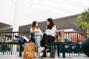 magnifique Jeune maman et adolescent fille sont en portant achats Sacs et souriant tandis que Faire achats dans centre commercial. famille achats. photo