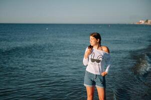 magnifique fille avec jolie jambes en marchant le long de le rivage dans le été chaud journée près le mer. photo