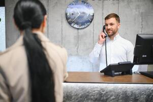 portrait de une Jeune Masculin réceptionniste dans une Hôtel hall portant une blanc chemise photo