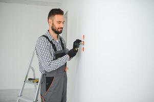 électricien constructeur à travail, installation de douilles et commutateurs. professionnel dans salopette avec un électricien outil. contre le Contexte de le réparation site photo