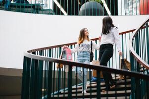 magnifique Jeune maman et adolescent fille sont en portant achats Sacs et souriant tandis que Faire achats dans centre commercial. famille achats photo