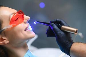 Jeune femme avoir dentaire remplissage séchage procédure avec guérir uv lumière à dentaire clinique photo