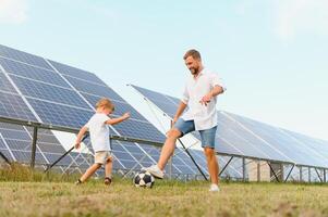 une père et le sien peu fils jouer Football près le solaire panneaux. le concept de renouvelable énergie. photo