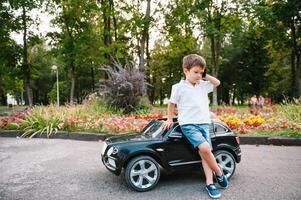 mignonne garçon dans équitation une noir électrique voiture dans le parc. marrant garçon monte sur une jouet électrique auto. copie espace. photo