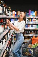 Jeune femme décider quoi du vin à acheter dans supermarché photo