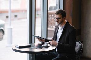 une homme séance dans une café avec tablette. décontractée homme en utilisant tablette ordinateur séance dans café surfant l'Internet photo