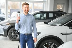 Jeune homme, vente électrique voitures dans le salle d'exposition. concept de achat respectueux de la nature voiture pour famille photo