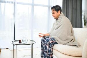 malade Indien homme dans plaid asseoir seul grelottant de froid. mauvais pour la santé arabe gars asseoir sur chaise sentiment malaise essayer à chauffage en haut photo