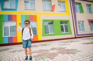 retour à école. content souriant garçon dans des lunettes est Aller à école pour le premier temps. enfant avec sac à dos et livre en plein air. début de cours. premier journée de tomber photo