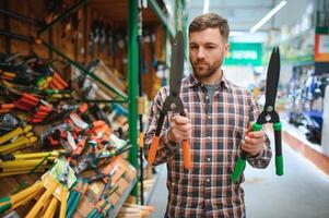 une homme choisit jardin cisailles dans une Matériel magasin. photo