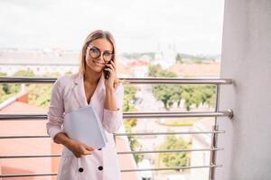 portrait de une charmant affaires femme bavardage sur sa intelligent téléphone tandis que attendre Quelqu'un dans café en plein air, magnifique femelle en utilisant mobile téléphone tandis que séance dans confortable restaurant dans le Frais air pendant. photo