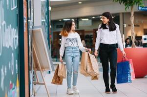 magnifique Jeune maman et adolescent fille sont en portant achats Sacs, achats dans centre commercial. famille achats photo