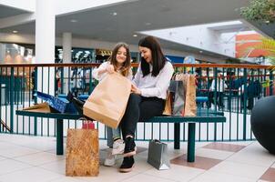 magnifique Jeune maman et adolescent fille sont en portant achats Sacs et souriant tandis que Faire achats dans centre commercial. famille achats photo