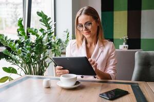 Jeune souriant femme d'affaires en buvant café et en utilisant tablette ordinateur dans une café magasin photo