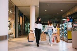 magnifique Jeune maman et adolescent fille sont en portant achats Sacs et souriant tandis que Faire achats dans centre commercial. famille achats photo