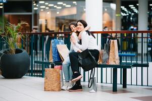 magnifique Jeune maman et adolescent fille sont en portant achats Sacs, achats dans centre commercial. famille achats photo