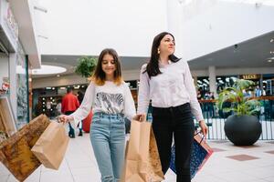 magnifique Jeune maman et adolescent fille sont en portant achats Sacs et souriant tandis que Faire achats dans centre commercial. famille achats photo