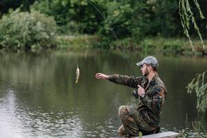 pêche dans rivière.a pêcheur avec une pêche barre sur le rivière banque. homme pêcheur captures une poisson pêche au brochet, filage bobine, poisson, breg rivières. - le concept de une rural partir. article à propos pêche photo