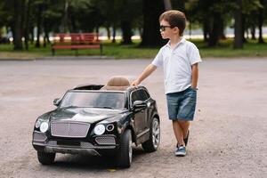 mignonne garçon dans équitation une noir électrique voiture dans le parc. marrant garçon monte sur une jouet électrique auto. copie espace. photo