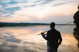 une pêcheur silhouette pêche à le coucher du soleil. eau fraiche pêche, capture de poisson. photo